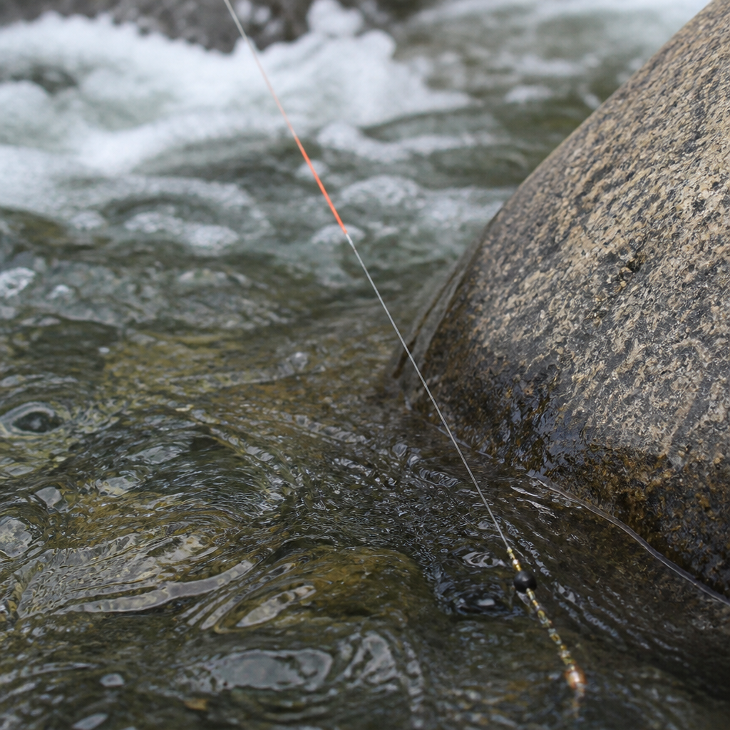 Close view of a leader with a coloured sighter section and two weighted nymphs entering fast clear water beside a boulder